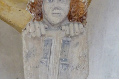 Gotski sklepnik v podobi mladeniča z dolgimi skodranimi lasmi, ki pred se boj drži ščit z dvema navzdol obrnjenima nožema – znak kamniškega strojarskega ceha.