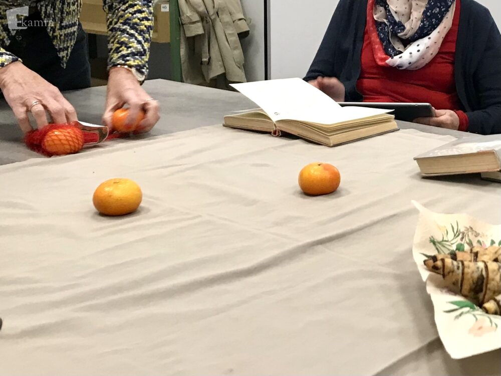 Članica pripravlja mizo za srečanje. Na prt je položila mandarine.